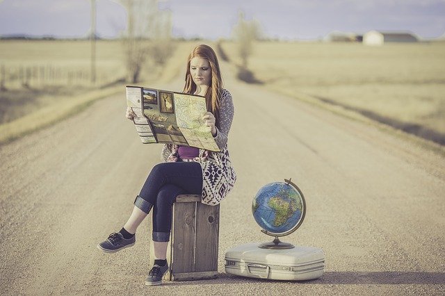 Kobieta z walizkami, mapą i globusem siedzi na polnej drodze